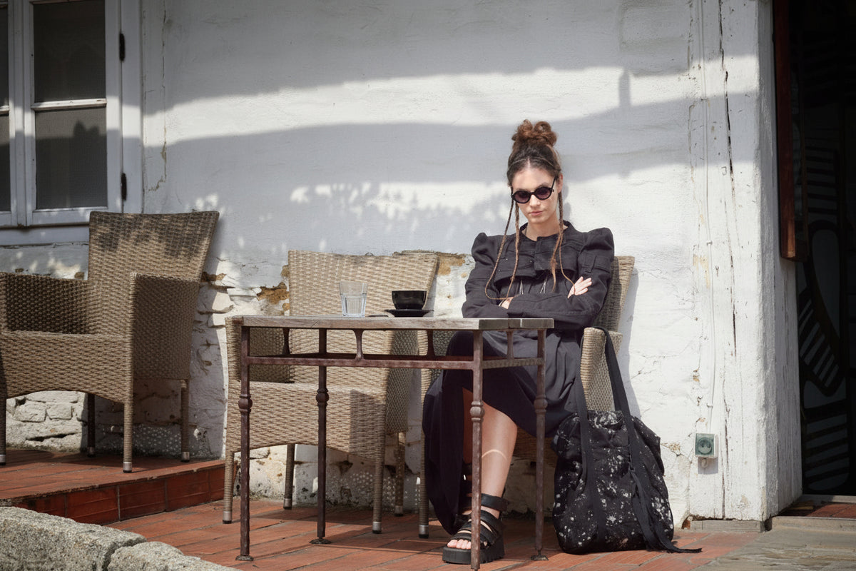 Woman sitting at a table outdoors with a white wall background